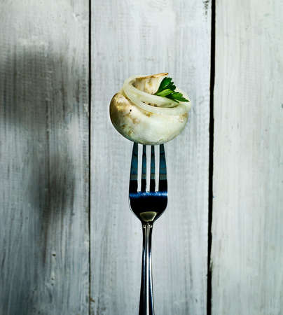 Fresh mushroom with onion and parsley on a fork. On white wooden backgroundの写真素材