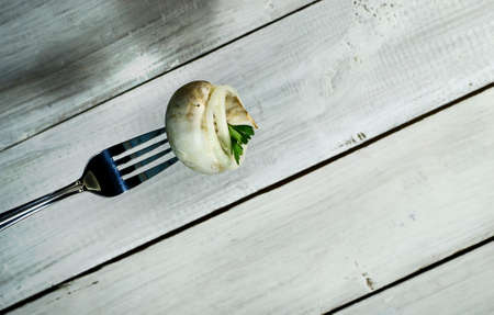 Fresh mushroom with onion and parsley on a fork. On white wooden backgroundの写真素材
