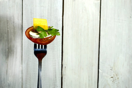 Ripe tomatoes with parsley, cheese and mushrooms on a fork. On white wooden backgroundの写真素材