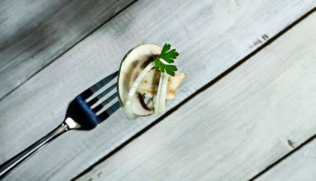 Fresh mushroom with onion and parsley on a fork. On white wooden backgroundの写真素材