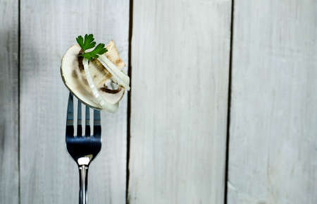 Fresh mushroom with onion and parsley on a fork. On white wooden backgroundの写真素材