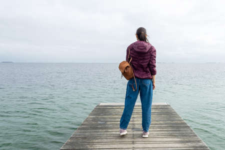 Girl with a backpack, looks at the sea, on a wooden pier. Freedom. Trips. Lifestyle.の写真素材