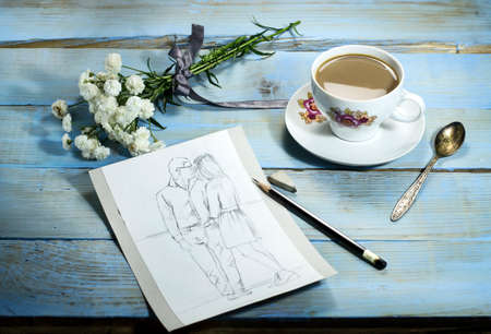 A sketch on wooden table with pencil, white flower and cup of coffeeの写真素材