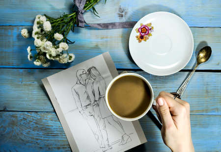 Top view of woman hand painting a sketch on wooden table with white flower and cup of coffeeの写真素材
