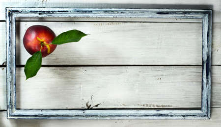 Nectarine with leaf in old frame on a white wooden backgroundの写真素材