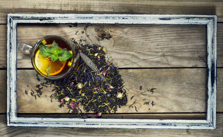 Cup of tea with lemon and mint in an old frame on a wooden background