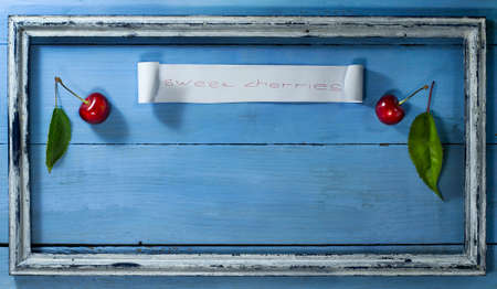 Cherries with leaves in old frame on a blue wooden backgroundの写真素材