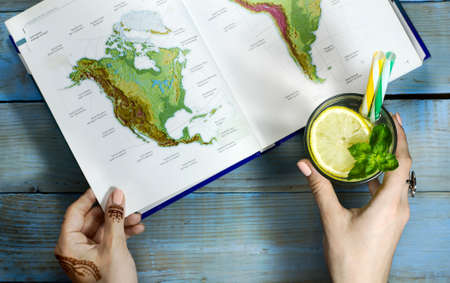 Top view of woman hand with lemonade, flower and geographic map on wooden tableの写真素材