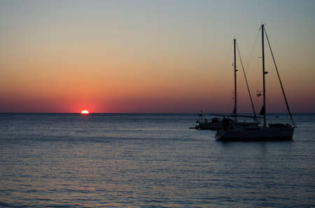 Silhouettes of yachts in the sea at sunset on a warm summer dayの写真素材