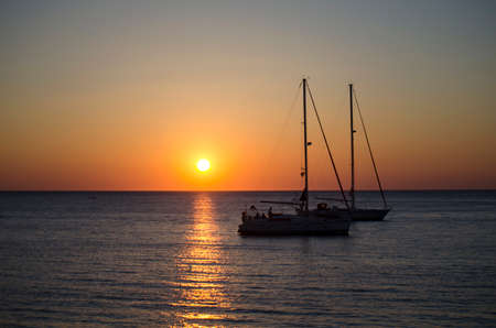 Silhouettes of yachts in the sea at sunset on a warm summer dayの写真素材