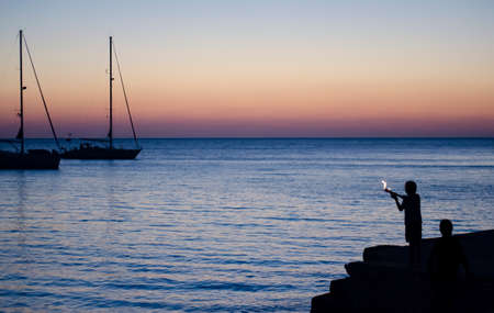 Silhouette of a boy with a torch on a background of sunset over the sea