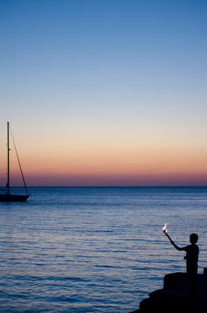 Silhouette of a boy with a torch on a background of sunset over the seaの写真素材