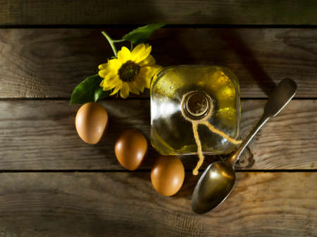 Sunflower oil in an old glass bottle with eggs and a spoon. On the wooden background with sunflowersの写真素材