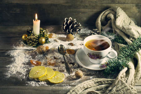 Cup of tea with lemon, dried apricots, raisins, warm scarf, with pine branches. Winter, New Year, Christmas still life. Wooden backgroundの写真素材