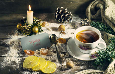 Cup of tea with lemon, dried apricots, raisins, warm scarf, with pine branches. Winter, New Year, Christmas still life. Wooden backgroundの写真素材