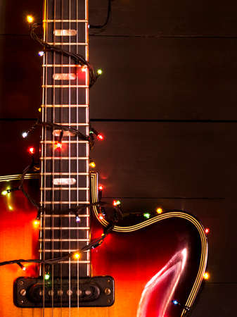 Old electric guitar with a lighted garland on a dark wooden background. Greeting, Christmas, New Year greeting card. Copy space.の写真素材