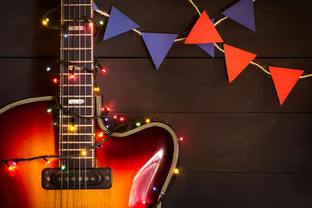Old electric guitar with a lighted garland on a dark wooden background. Greeting, Christmas, New Year greeting card. Copy space.の写真素材