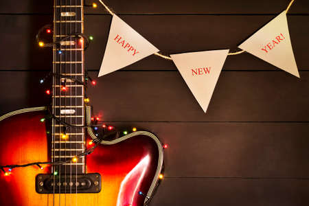 Old electric guitar with a lighted garland on a dark wooden background. Greeting, Christmas, New Year greeting card. Copy space.の写真素材