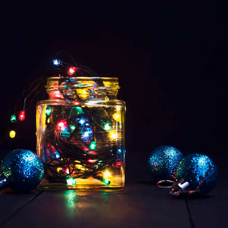 A glowing garland in a glass jar and Christmas decorations on a dark wooden background. New Year, Christmas postcard. Copy space. Holiday backgroundの写真素材