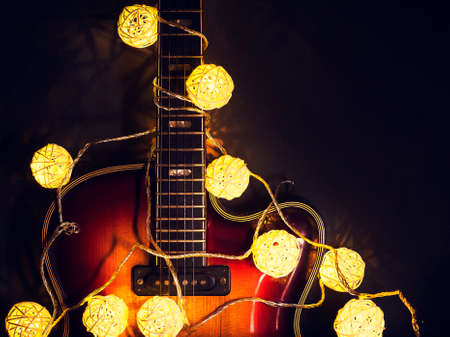 Old electric guitar with a lighted garland on a dark wooden background. Greeting, Christmas, New Year greeting card. Copy space.の写真素材