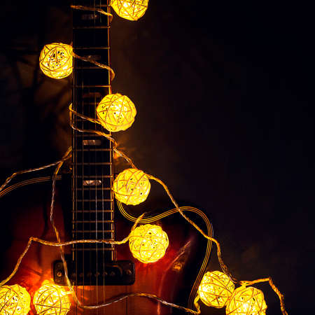 Old electric guitar with a lighted garland on a dark wooden background. Greeting, Christmas, New Year greeting card. Copy space.の写真素材