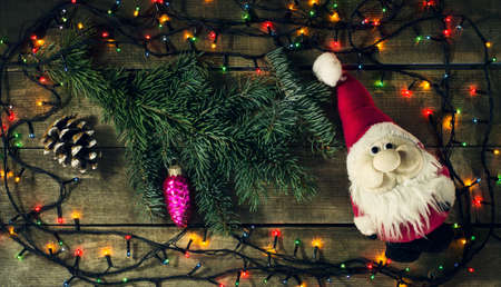 Glowing Christmas tree garland with presents and Santa Claus toy on a wooden backgroundの写真素材