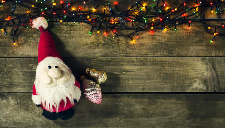 Glowing Christmas tree garland with presents and Santa Claus toy on a wooden backgroundの写真素材