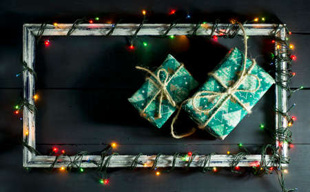 Glowing Christmas tree garland on old frame with decorations and gifts. On a blue wooden background.の写真素材