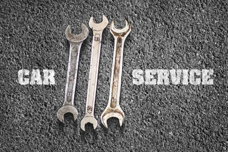Car service concept. Inscription Car service and wrenches against the backdrop of black asphalt....