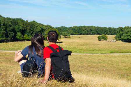 Young couple are sitting on the grass and looking at a beautiful landscape. Concept travel. Summer. Sunny day.の写真素材