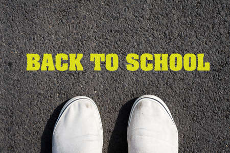 Two white sneakers on black asphalt. The inscription Back to school. The concept of education. View from above. Background.の写真素材