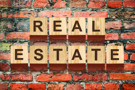 Real Estate, inscription from the alphabet on wooden cubes on the old brick wall. Business Background.の写真素材