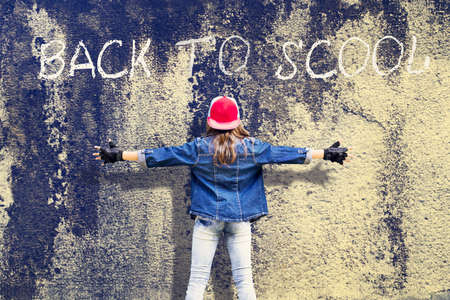 Girl teenager with widely apart hands. Denim clothing. Baseball cap. Against the background of the old concrete wall. Inscription Back to School. Education. Backgroundの写真素材