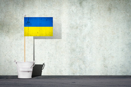 Flag of Ukraine, on a stick, in a small bucket, against the background of a concrete wall. Copy space. Signs and Symbols. Flags.の写真素材