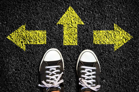 Sneakers on an asphalt road. Yellow arrows pointing in different directions. View from above. The concept of choosing the right path. Business. Lifestyle. Background.の写真素材