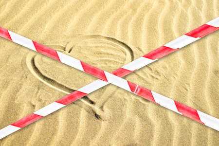 The contour of the heart on a sandy beach is crossed out with a barrier tape. Coronavirus. COVID 19. Pandemic. Beaches Quarantined. closed entrance to the beaches.の写真素材