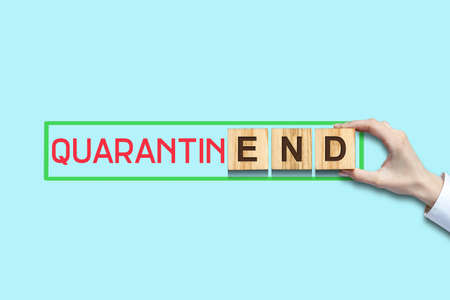 End of quarantine. Female hand makes up the inscription on wooden blocks on a blue background. The end of the pandemic. Opening a business.の写真素材