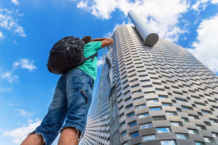 Copenhagen. Denmark. July 23, 2019: Man with a backpack looks at the facade of a modern metal building against a cloudy sky. Bottom view. Power station in the city of Copenhagen, Sights.のeditorial素材
