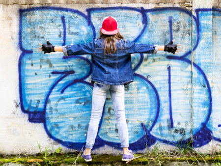 Cute young fair-haired girl teenager in a baseball cap and denim shirt on a stone wall background.の写真素材