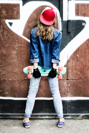Cute girl in a baseball cap with a skateboard on a dark background.Sport. Healthy lifestyle.の写真素材