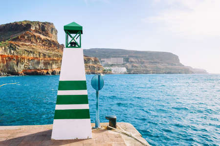 Small lighthouse on the quay. against the background of the ocean, beautiful mountains and a cloudy...