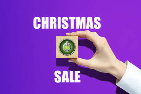 Christmas sale. Power button, on a wooden block in a woman's hand. Purple background. Festive concept of starting sales. Business. Holidays.の写真素材