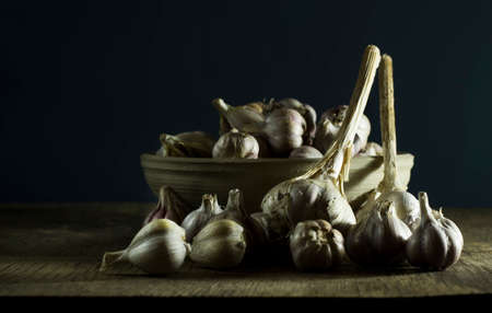 Heads of garlic in a bowl on the old wooden background.