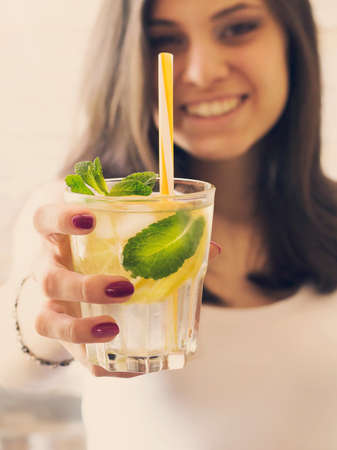 A glass of detox water with lemon, ice and fresh mint in the hands of a young girl. Healthy lifestyle.の写真素材