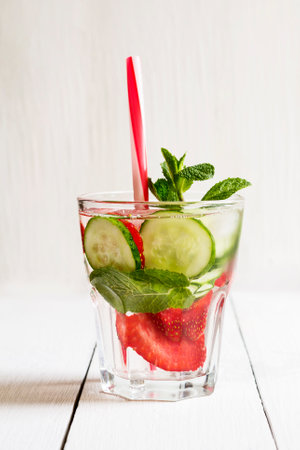 A glass of detox water with strawberries, ice and fresh cucumber. Healthy lifestyle.White wooden background.の写真素材