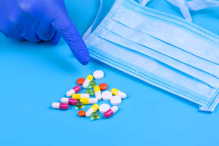 Hand in a medical glove points to different pills on a blue background. Medicine. Treatment....