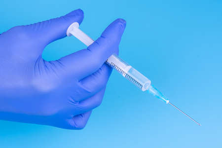 Hand in a medical glove with a syringe on a blue background. Close-up. Vaccinations. Medicine....