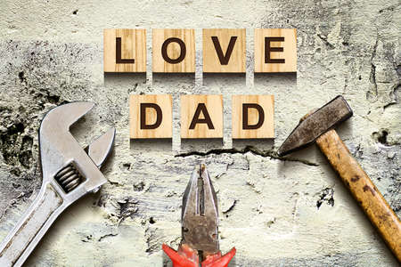 Love Dad inscription on wooden cubes with working tools on an old vintage concrete wall. Happy Father's Day Concept. Greetings and gifts. Holidays.の写真素材