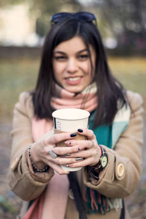 Young beautiful girl with a coffee in a paper cup. Against the background of the autumn parkの写真素材