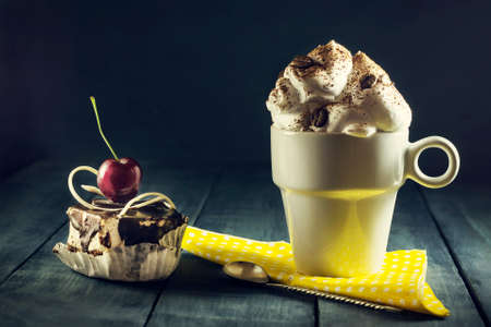 Chocolate cake with cherries and a cup of coffee with whipped cream. Wooden dark blue background